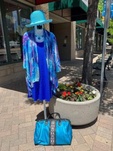 What are the best stylish clothes to wear on a long flight?- Accessories with a flair...and hair - Greeley's women's clothing boutique travel wear - picture of a mannequin wearing a blue Wallaroo hat paired with a blue wrinkle-free dress and cardigan