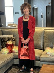How Can I Make My Simple Black Dress Look Festive? - A pretty woman wearing a sparkly red long jacket, holding a gift.